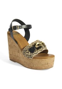 Sandale compensée avec une base en liège, une bride de cheville en cuir noir et une tige en paille tissée avec un accent en cuir noir et des éléments en or.