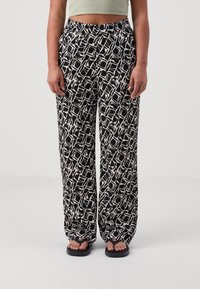 Pantaloni a gamba larga a fantasia bianca e nera con una cintura elastica e un tessuto morbido, caratterizzati da un design geometrico e una vestibilità rilassata.