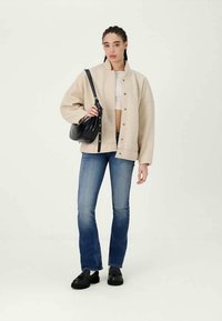 Beige oversized jacket, white top, blue flared jeans, and black shoes. Black shoulder bag with adjustable strap. Simple, modern design.