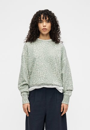 Hellgrünes Sweatshirt mit Leopardenmuster, langen Ärmeln und gerippten Bündchen, kombiniert mit einem weißen, geschichteten Oberteil und dunkler Hose. Weiche Textur.