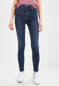 Jeans de mezclilla azul de cintura alta con corte ajustado, que cuentan con un diseño de cinco bolsillos y detalles de costura sutiles. Cintura estándar y longitud hasta el tobillo.