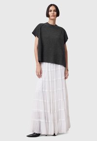 Maglione oversize grigio scuro lavorato a maglia con maniche corte, abbinato a una gonna maxi bianca a balze. Stivaletti neri con punta a punta completano il look.