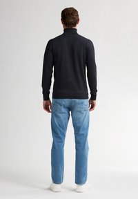 Granatowy sweter z golfem o dopasowanym kroju i prążkowanymi mankietami, połączony z jasnoniebieskimi dżinsami i białymi trampkami, pokazany od tyłu.