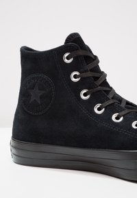 Černé vysoké semišové tenisky Converse s černými tkaničkami, stříbrnými očky a vyraženým logem na kotníku.
