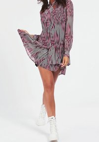 Vestido de manga larga con un patrón de pata de gallo en negro, blanco y rosa, cintura fruncida, falda fluida, combinado con botas blancas de cordones hasta el tobillo.