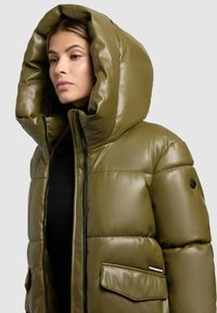 Gefütterte olivgrüne Jacke mit einer großen, strukturierten Kapuze, glänzender Oberfläche, Frontreißverschluss und seitlichen Taschen. Texturiertes Material mit sichtbaren Nähten.
