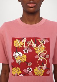 Rosa bomull t-skjorte med et rødt blomsterdesign med gule og rosa blomster, en slange og brodert tekst "MAX". Korte ermer og rund hals.