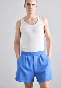 Top blanco sin mangas y shorts azules con una ancha cinturilla elástica, que cuentan con bolsillos laterales y un material de algodón texturizado.