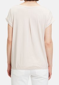 Jasno beżowa bluzka krótki rękaw o luźnym kroju z plisą z tyłu. Miękka tkanina, okrągły dekolt i podwinięte rękawy.