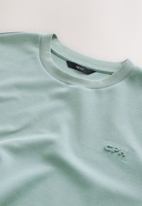 Mintgroen katoenen T-shirt met een ronde hals en korte mouwen, met een tonale "CPH"-logo aan de voorkant. Zachte textuur, casual ontwerp.