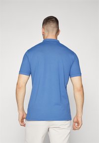 Polo azul de manga curta com colarinho clássico, textura suave e bainha reta, usado com calças de tom claro.