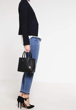 Černá textura kabelky s dvojitými uchy, malý detail visacího zámku, kombinovaná s tmavým sakem, bílou košilí a distressed modrými džíny.