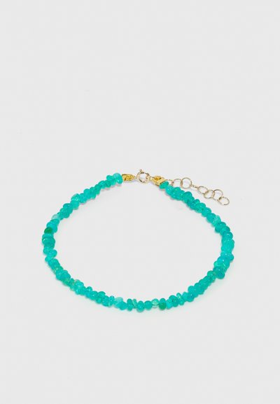 Bracciale in perle turchesi con pietre di forma irregolare e finitura lucida, fissato con componenti metallici tono oro e una catena regolabile.
