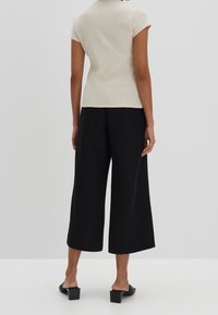 Beżowy prążkowany top z krótkim rękawem w połączeniu z czarnymi szerokimi spodniami o kroju 7/8. Model nosi czarne mules na obcasie blokowym, prezentując luźną sylwetkę.