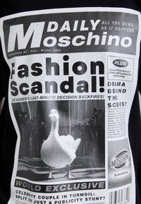 Fekete póló újságstílusú grafikával. A tervezés élénk fehér szöveget és egy liba képet tartalmaz, pixelhatásokkal.