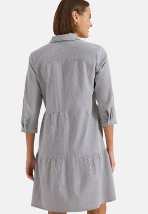 Femme portant une robe à rayures verticales noires et blanches, longueur genou, avec manches 3/4 et col, posant de dos à la caméra.