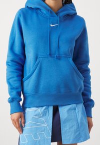 Blå sweatshirt med huva, framficka och elastiska ärmslut. Har en vit Nike-logotyp på bröstet. Mjuk bomullsblandning.
