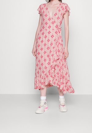 Kvinde iført en lyserød blomsterprint slå-om kjole med flæsekant og korte ærmer, kombineret med hvide sokker og hvide sneakers med lyserøde detaljer.