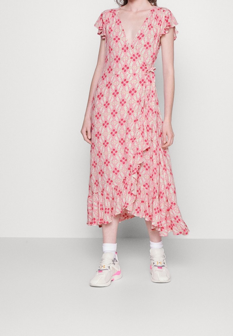 Femme portant une robe portefeuille rose à fleurs, ourlet à volants et manches courtes, associée à des chaussettes blanches et des baskets blanches avec des touches roses.