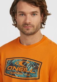 Orange cotton t-shirt featuring a graphic design with palm leaves and the text "O'Neill California U.S.A." on the front.
