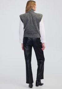 Szary wełniany kamizelka z wysokim kołnierzem, zestawiona z czarnymi skórzanymi spodniami. Posiada akcentowane ramiona i prążkowany dół. Gładka tekstura całości.