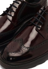 Zapatos de cuero burdeos pulidos con detalles de brogue, cordones negros y una suela texturizada con un borde estampado.