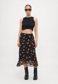 Svart blomstermønstret omslagsskjørt med gjennomsiktig kant, sammen med en tettsittende svart croptop og svarte knesokker. Har levende blomsterdesign.