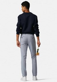 Helle graue Hose im Slim Fit mit Gesäßtaschen und glatter Textur, kombiniert mit einem dunkelblauen Sweatshirt. Weiße Sneakers vervollständigen den Look.