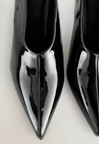 Zapatos de punta afilada de charol negro con una superficie suave y brillante y un detalle de costura central. Diseño elegante con un escote bajo en el empeine.