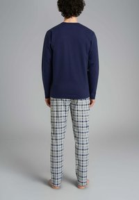 Maglietta a maniche lunghe navy con collo tondo abbinata a pantaloni a quadri chiari in tonalità di blu e beige. Il materiale sembra morbido e comodo.