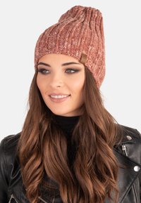 Gorro de punto en tonos rosas, con textura acanalada y una parte superior holgada. Incluye una sutil etiqueta de cuero en el costado. Material suave.