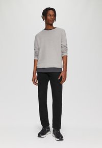 Grijze longsleeve sweatshirt gelaagd over een zwart shirt, gecombineerd met zwarte cargobroek en zwarte sportieve schoenen. Eenvoudig ontwerp, geen patronen.