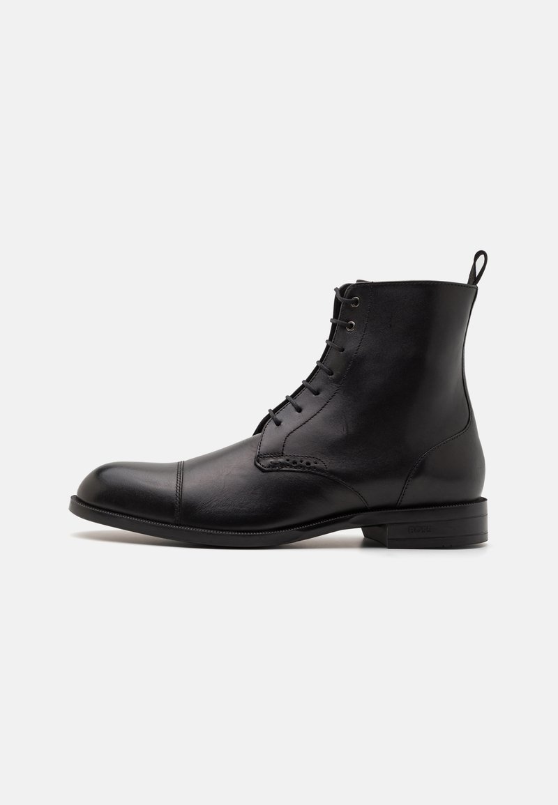Sorte lær ankle boot med rund tå, snøring foran og en liten løfteløkke. Glatt tekstur med subtile sømdetaljer.