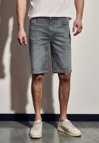 Harmaat farkkushortsit suoran leikkauksen, viiden taskun, haalistuneen pinnan ja kääntöhelmojen kanssa, yhdistettynä valkoisiin tennareihin.