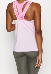 Różowy sportowy top na ramiączkach typu racerback z białymi paskami ozdobionymi różowym napisem "NIKE". Lekka tkanina o gładkiej fakturze.