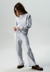 Light gray sweatshirt with embroidered "PARIS" and wide-leg gray sweatpants. Brown shoes complete the outfit. Simple, casual design.