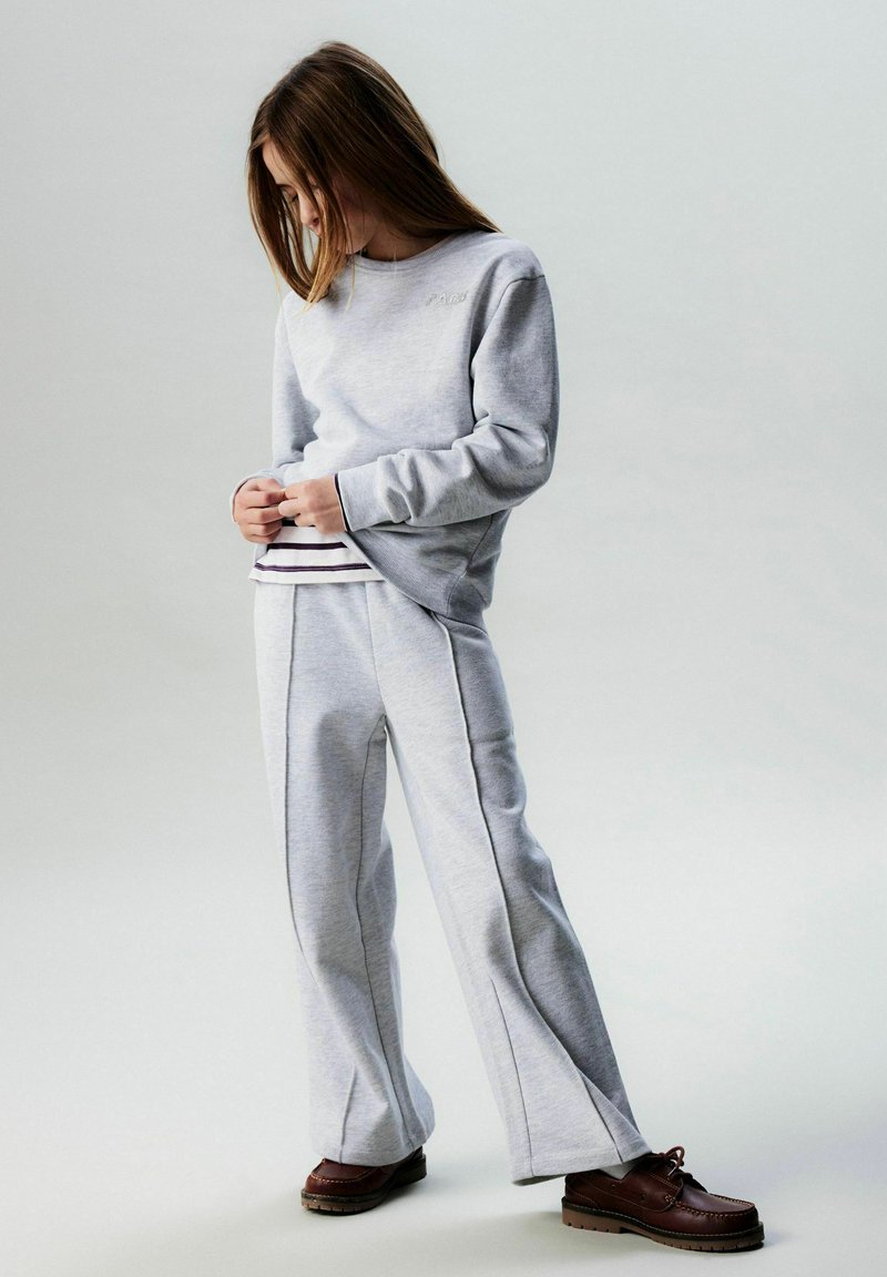 Felpa grigio chiaro con "PARIS" ricamato e pantaloni della tuta grigi a gamba larga. Scarpe marroni completano l'outfit. Design semplice e casual.