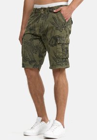 Olivgrön cargoshorts med svart blommönster, knäppning och dragkedja, justerbart midjeband och sidofickor. Matchas med vita sneakers.
