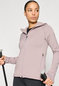 Casaco roxo claro com fecho de correr e capuz, confeccionado em material macio, apresenta bolsos laterais com fecho e um design atlético.