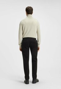 Kremowy sweter z golfem i czarne spodnie z kordurowej tkaniny, noszone z ciemnym obuwiem. Sweter ma prążkowane mankiety i dopasowany krój.