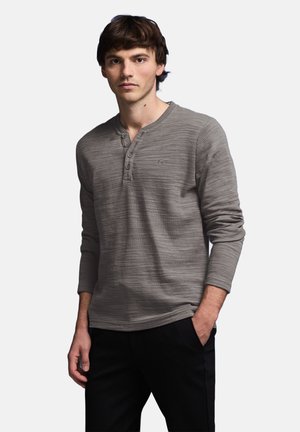 Grå langærmet henley skjorte med et subtilt tekstureret mønster, med en rund halsudskæring og tre-knaps placket, parret med mørke bukser.