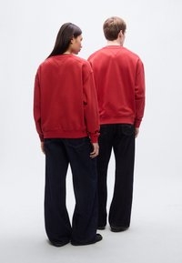 Κόκκινα βαμβακερά φούτερ με ριμπ μανσέτες και τελείωμα, συνδυασμένα με φαρδιά σκούρα τζιν τζιν. Η εικόνα δείχνει τους φορείς από πίσω.