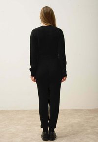 Svart stickad tröja med ribbad mönster, tillsammans med matchande svarta byxor. Slät textur, figurnära design och enhetlig färg genom hela plagget.