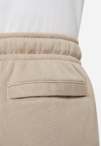 Béžové tepláky s texturovaným pasem, obsahující prošitou kapsu na zadní straně a měkkou látkou pro pohodlí.