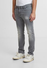 Jeans de denim gris con un ajuste slim, textura desgastada y diseño de cinco bolsillos. Combinados con zapatillas blancas con acentos grises.