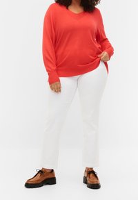 Pull rouge à manches longues avec col en V, associé à un pantalon blanc à jambes droites et des chaussures marron à lacets avec une semelle épaisse. Détails minimalistes.