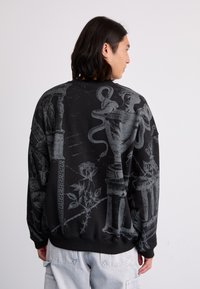Black sweatshirt featuring detailed gray graphic prints of classical elements, including vases, snakes, and a rose. Crew neck and relaxed fit.