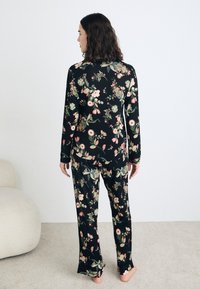 Zwart pyjamastel met een floral patroon en roze en groene accenten. Lange mouwen en losse broekspijpen, gemaakt van zachte stof.