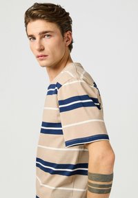 Camisa de manga corta a rayas beige con franjas horizontales en azul marino y blanco. Fabricada en algodón, con un escote redondo y un corte relajado.