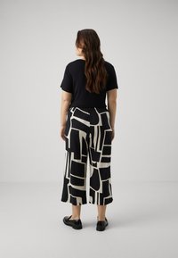 Haut noir, large culottes noires et blanches à motifs, tissu lisse avec des designs géométriques, et chaussures noires à enfiler.